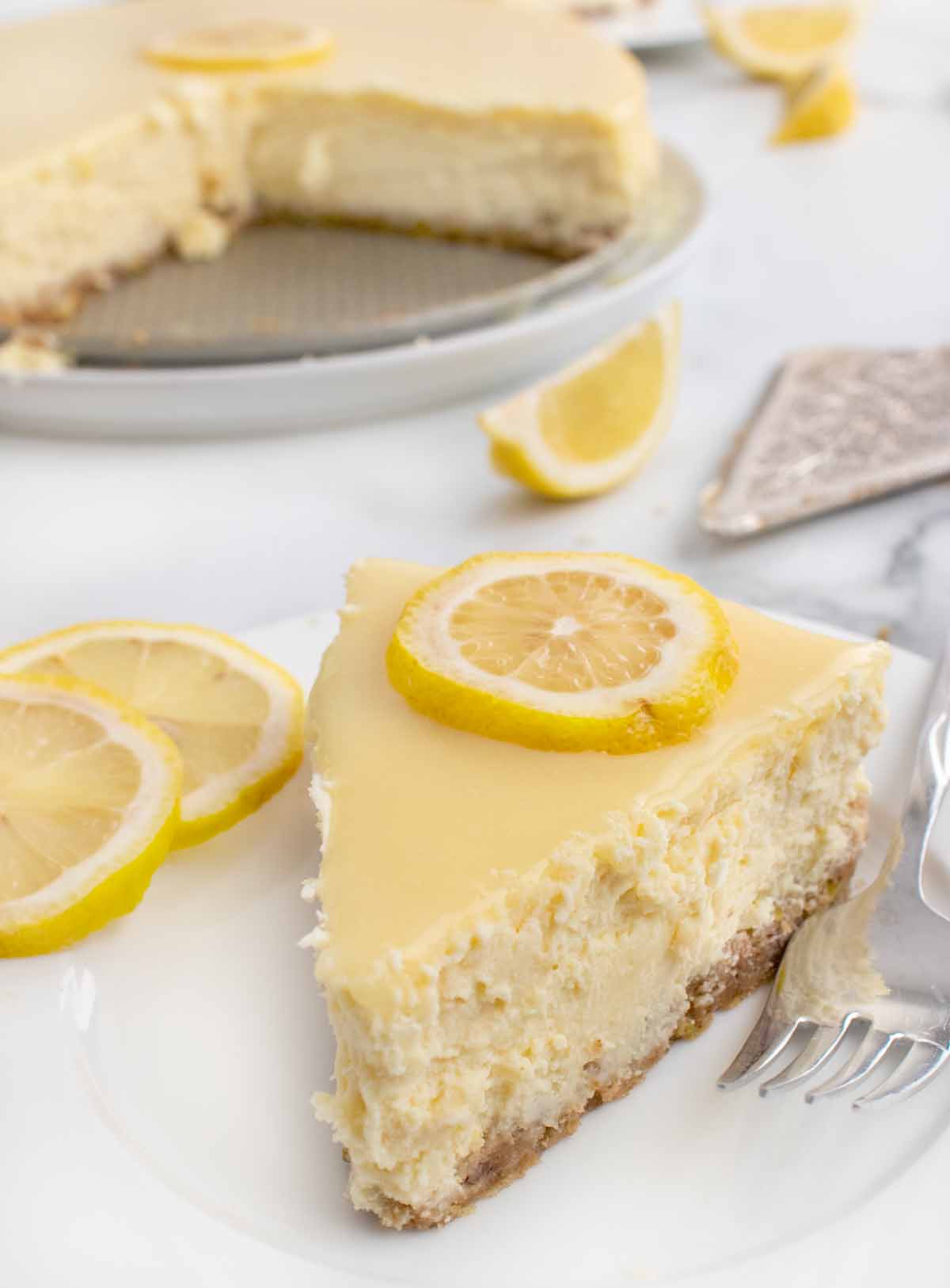 slice of lemon cheesecake on a white plate with sliced lemons and a fork