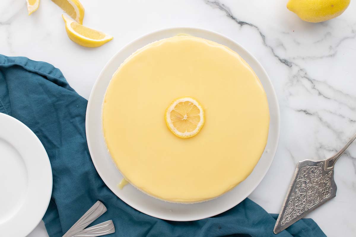 whole cheesecake on a white platter with a spatula, blue napkin, and lemons around it