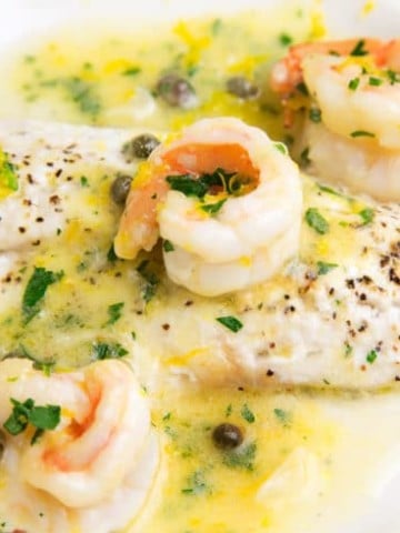 black seas bass topped with shrimp in a lemon caper sauce on a white plate