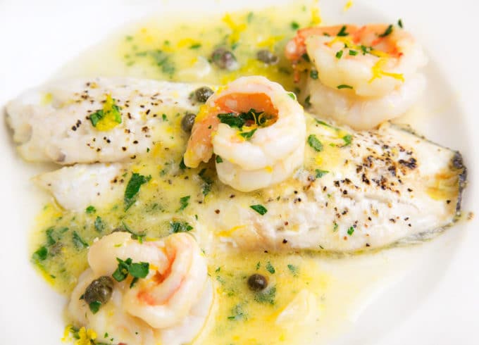 black seas bass topped with shrimp in a lemon caper sauce on a white plate