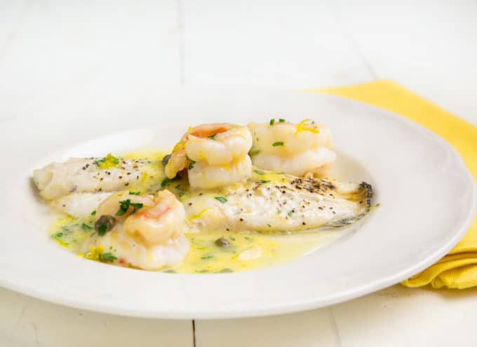 black seas bass topped with shrimp in a lemon caper sauce on a white plate