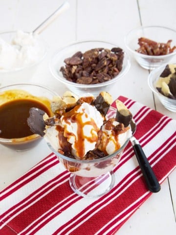 candied maple bacon sundae on a red and white striped napkin with bowls of the ingredients