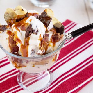 candied maple bacon sundae in a glass dish with a spoon and a striped red and white napkin under the dish