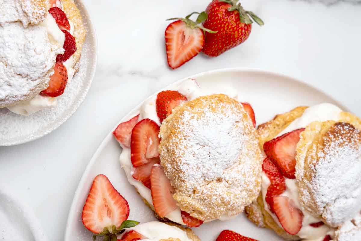 individual strawberry shortcakes on a white platter with sliced strawberries around the platter