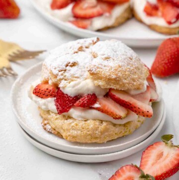 individual strawberry shortcake on a white plate with strawberries around the plate