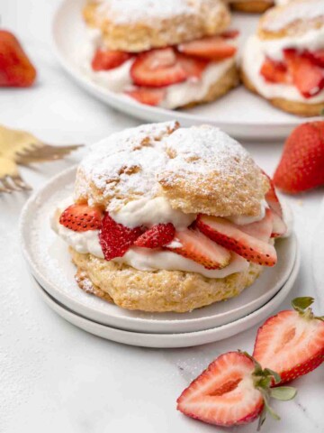 individual strawberry shortcake on a white plate with strawberries around the plate