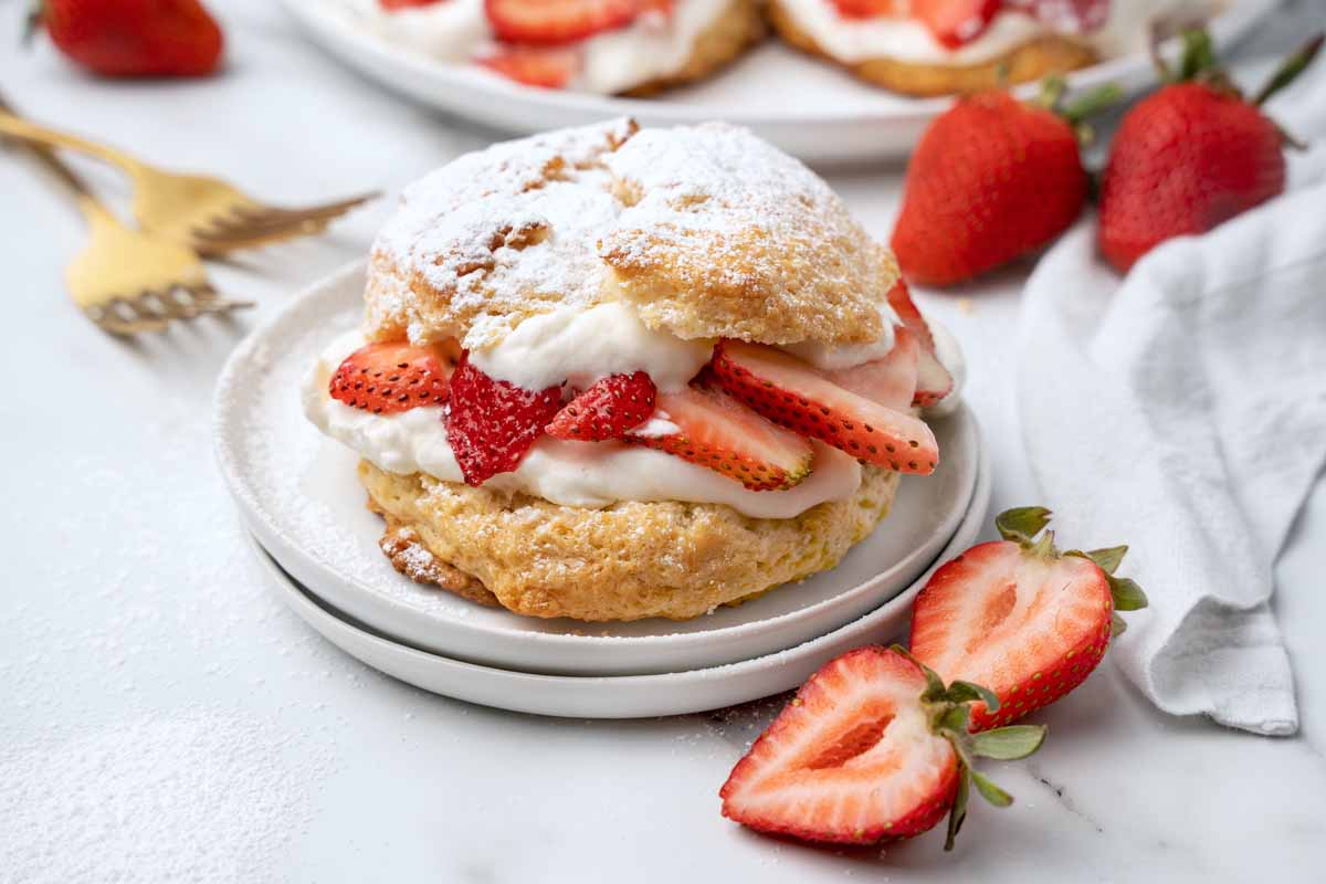 individual strawberry shortcake on a white plate with strawberries around the plate