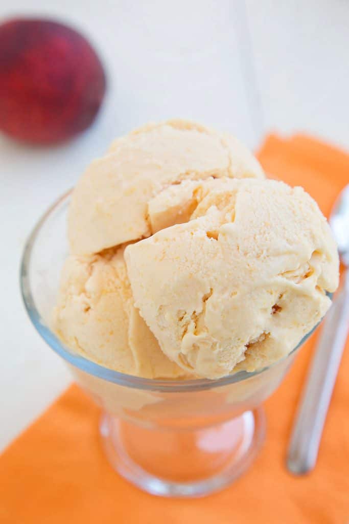 close up of grilled peaches and cream gelato in a glass dish on a tangerine colored napkin with a spoon