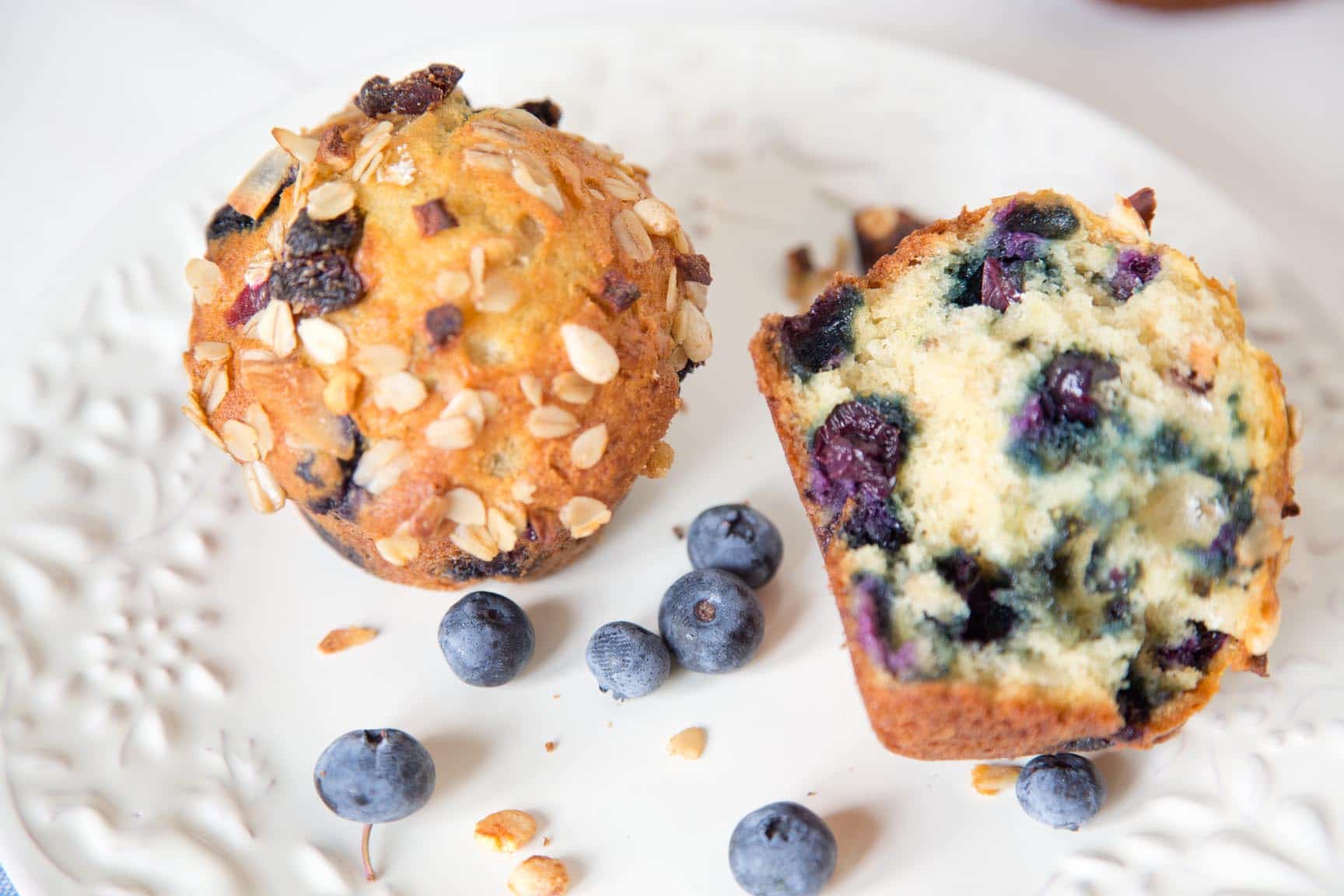 one  and one half Blueberry muesli muffins on a white plate with blueberries