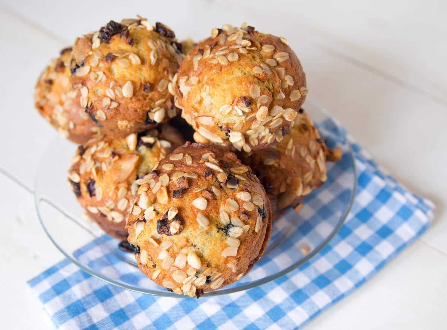 stack of Blueberry muesli muffins on a clear glass plate with a blue and white checkered napkin under the plate