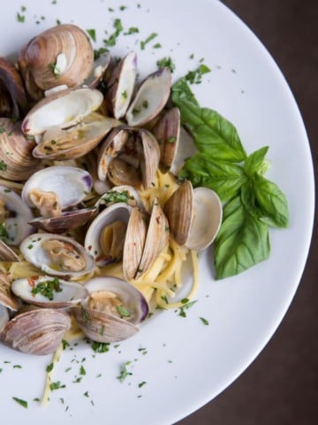 white bowl with steamed clams on linguine with a sprig of basil