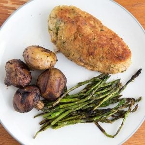 overhead view of cooked breaded stuffed pork  with grilled mushrooms and asparagus on a white plate