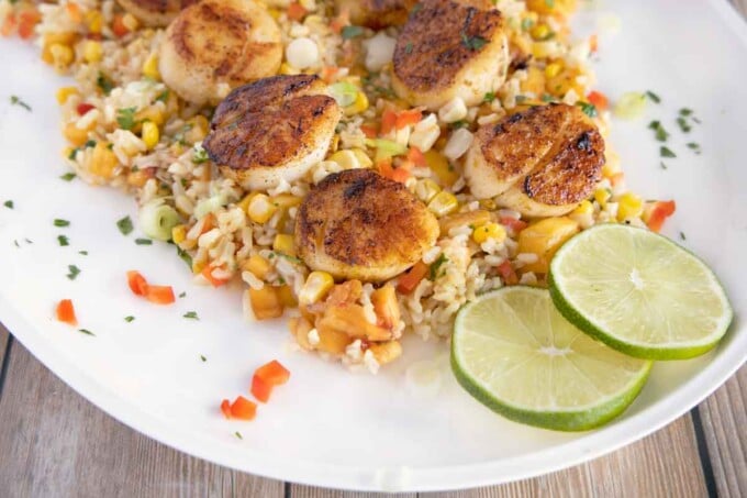 pan-seared scallops on a bed of rice with peaches and corn on a white oval platter