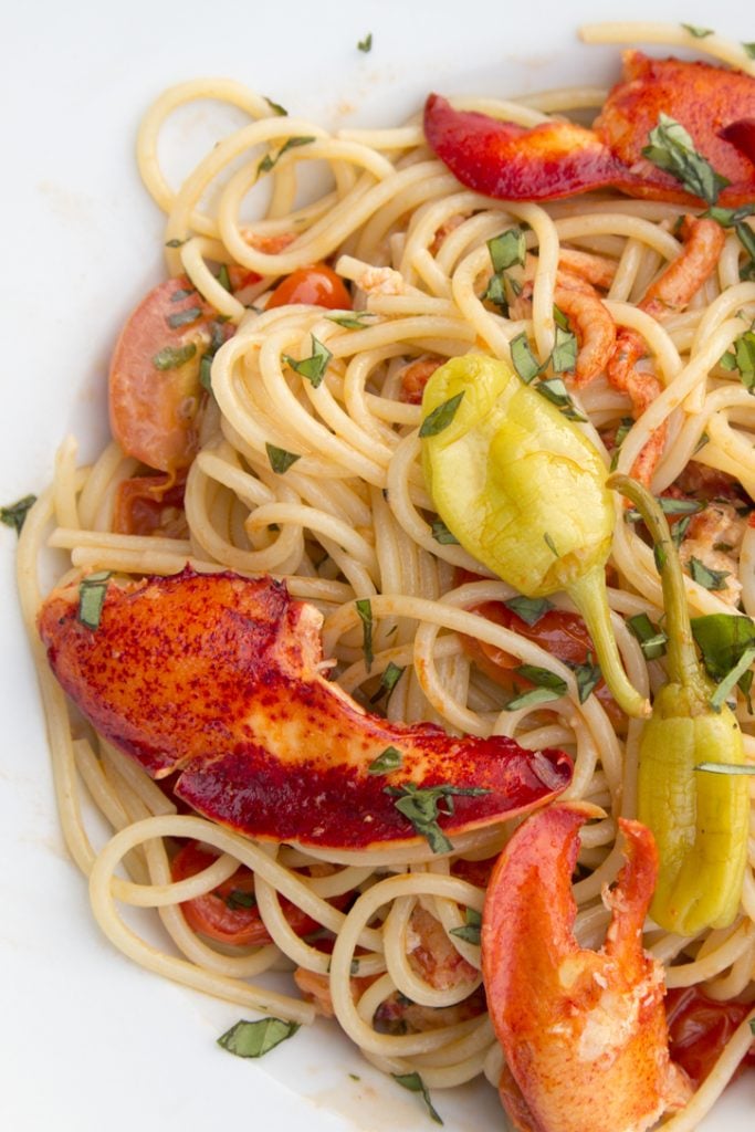 overhead partial shot of lobster claws and lobster meal with pepperoncini over pasta with chopped basil 