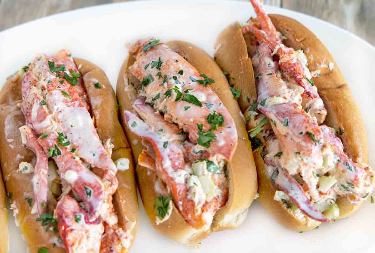 3 lobster rolls on a white platter.