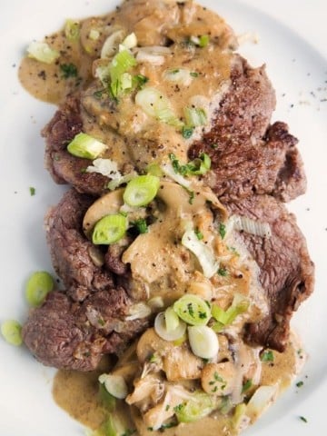 A white plate with filet slices topped with Steak Diane Sauce
