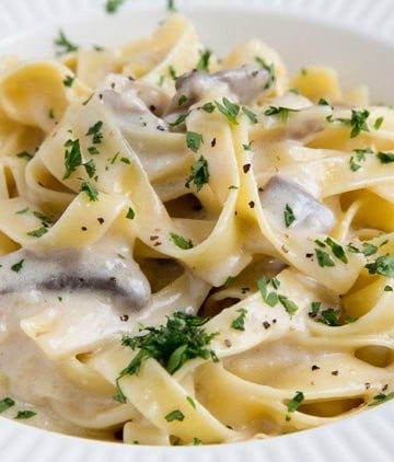 fettuccine alfredo in a white bowl sprinkled with parsely