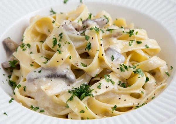 Fettuccine Alfredo sprinkled with parsley in a white bowl.