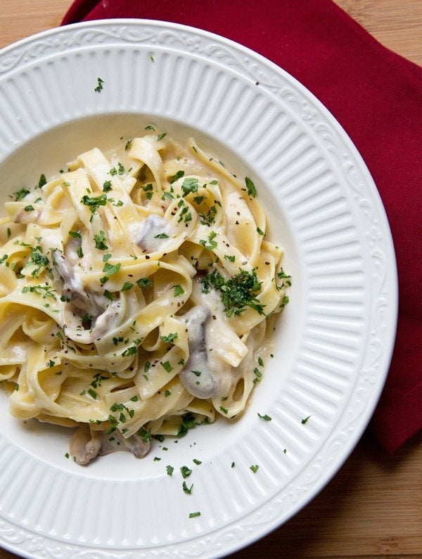 Fettuccine Alfredo in a white bowl on a red napkin sitting on a cutting board.