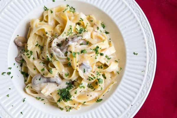 Overhead shot of Fettuccine Alfredo in a white bowl sitting on a red napkin