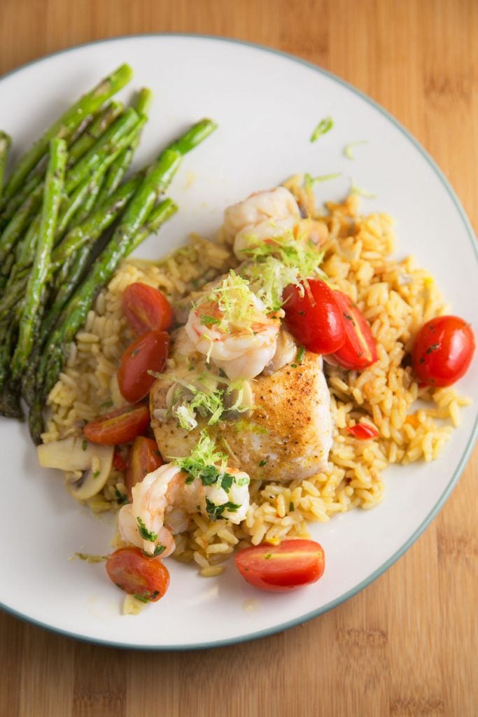 overhead shot of pan seared red snapper and shrimp on a bed of rice with grape tomatoes and a side of asparagus