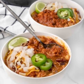 chicken chili with cheese, sliced jalapenos and lime wedge in a white bowl.