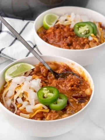 chicken chili with cheese, sliced jalapenos and lime wedge in a white bowl.