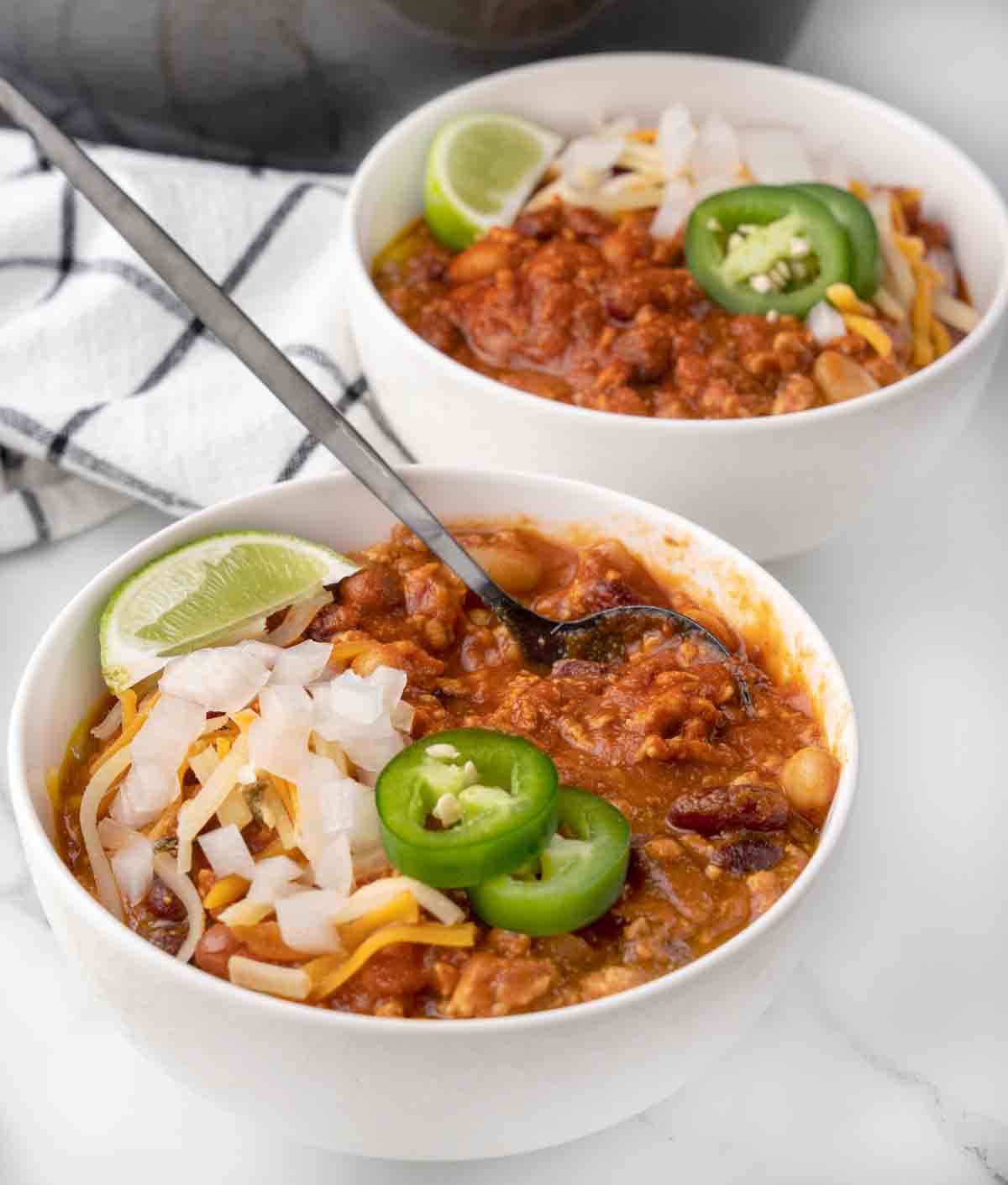 chicken chili with cheese, sliced jalapenos and lime wedge in a white bowl.