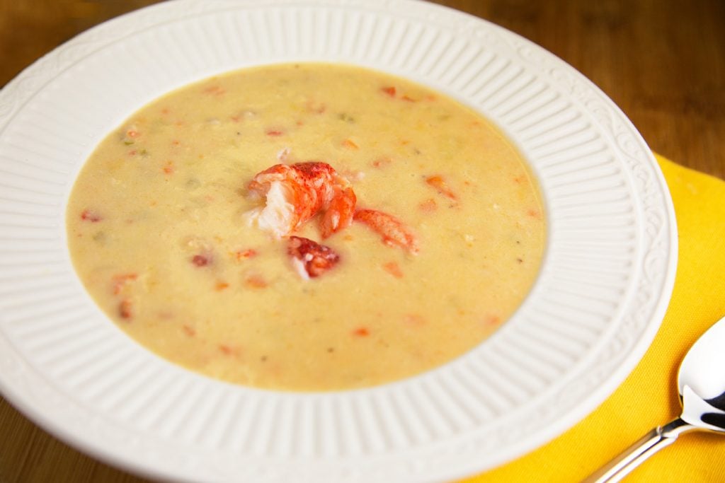 lobster chowder with lobster meat on top in a white bowl, next to a lemon yellow napkin with a spoon