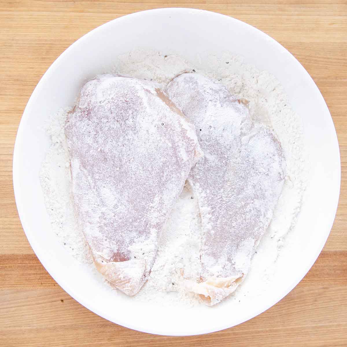 chicken coated in flour in a white bowl of flour