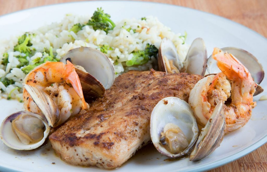 blackened fish, clams and shrimp on a white plate with rice and broccoli