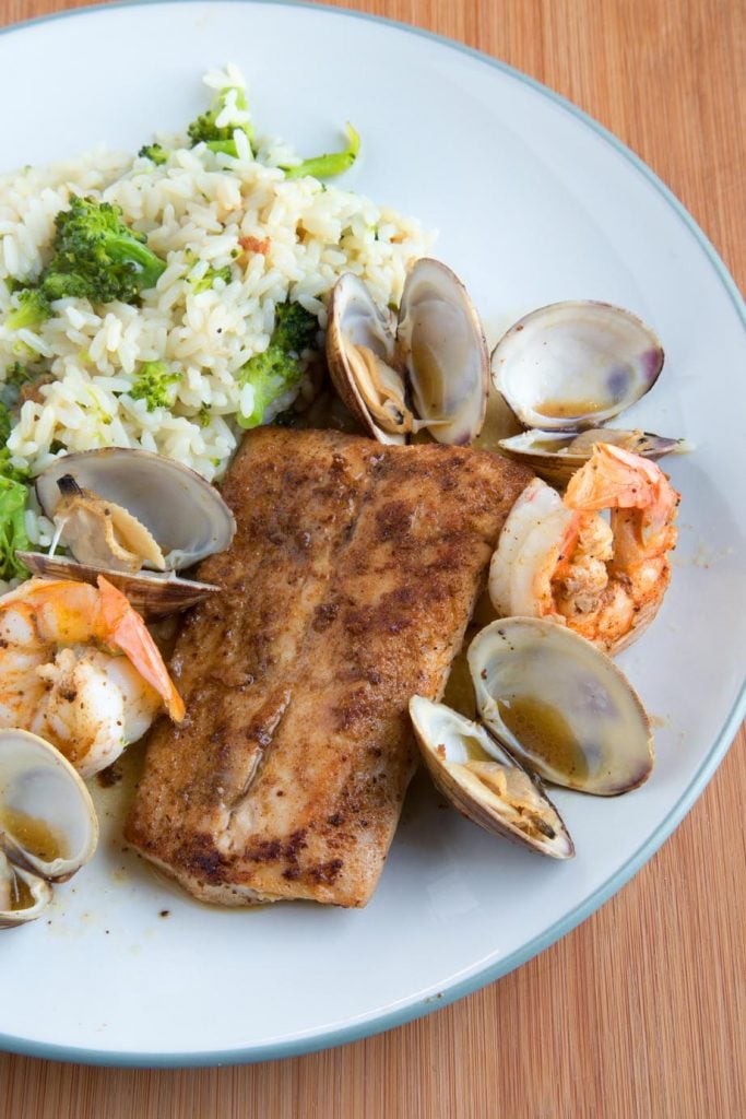 overhead view of Baltimore Clam Bake with blackened fish, clams and shrimp on a white plate with rice and broccoli