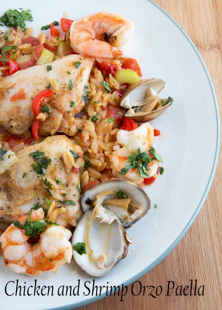 An overhead view of Chicken and Shrimp Orzo Paella on a green rimmed off white plate on a wooden cutting board