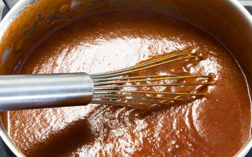 overhead view of Enchilada Red Sauce in a pot with a wire whisk in the sauce