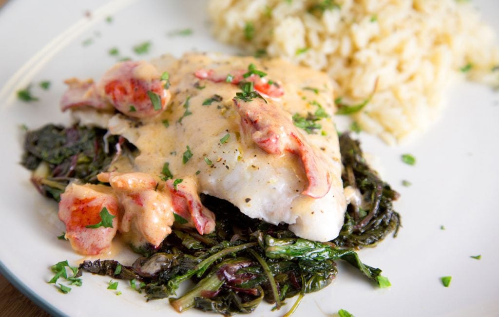 red snapper on greens with a lobster cream sauce and a side of rice on a white plate