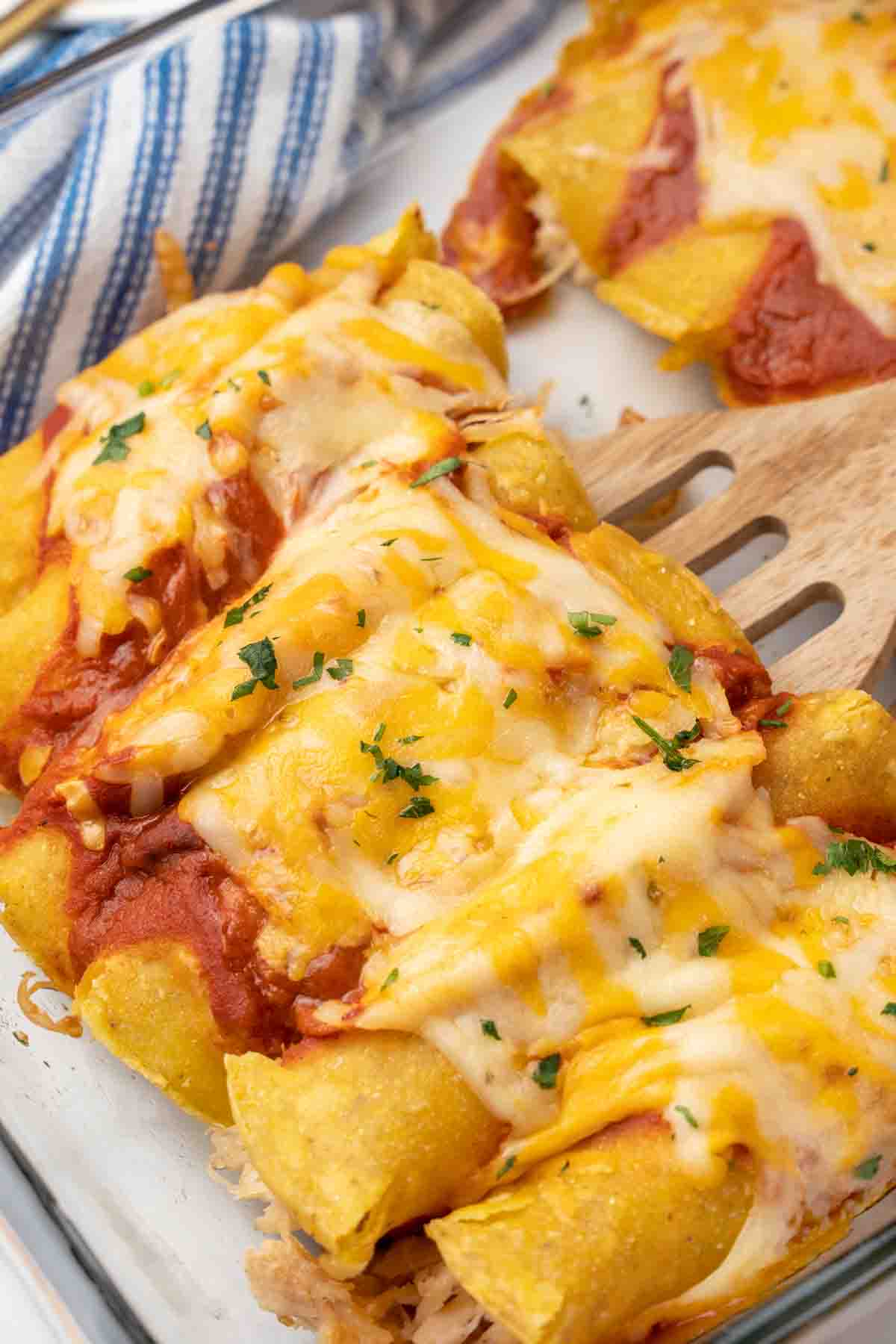 Tex-Mex chicken enchiladas being lifted out of baking dish with spatula.