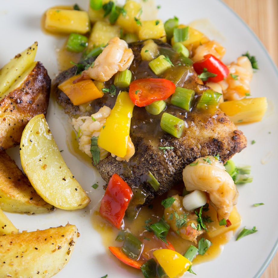 overhead view of blackened mahi-mahi with pineapple lobster sauce on a white plate next to seasoned potatoes