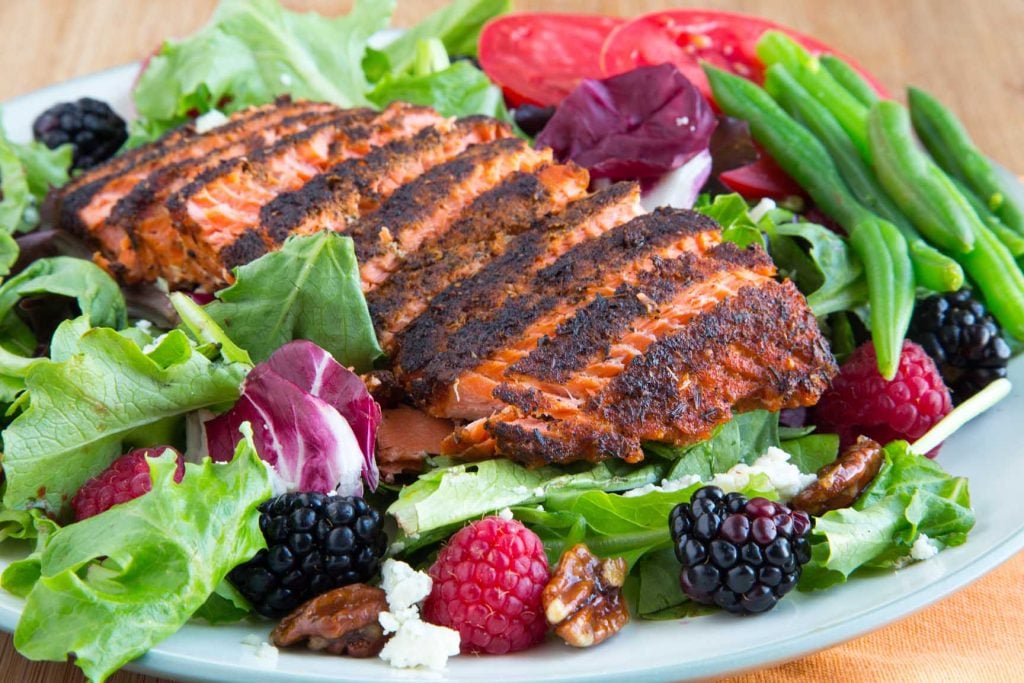 sliced filet of blackened salmon on a bed of lettuce with berries, nuts, green bean sand tomatoes