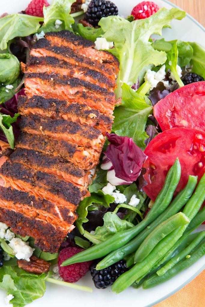 overhead partial view of sliced filet of blackened salmon on a bed of lettuce with berries, nuts, green bean sand tomatoes