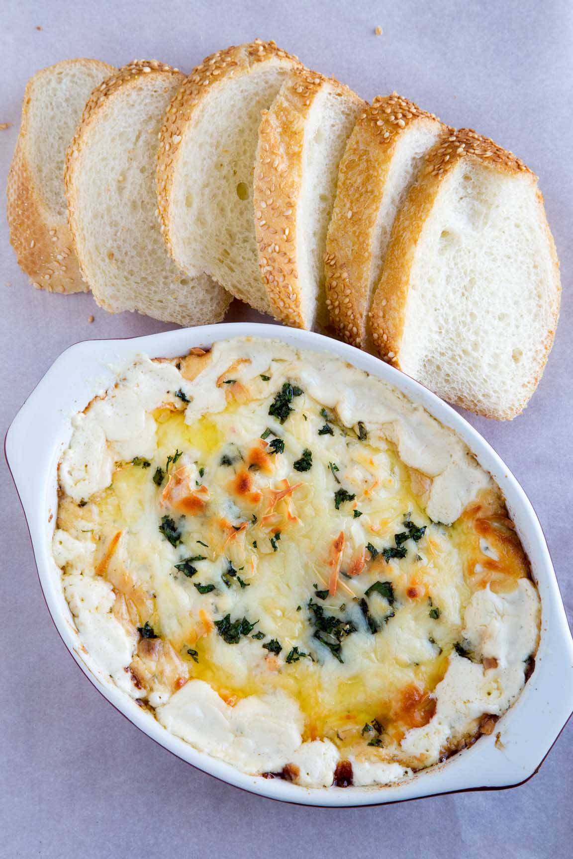 Shrimp Scampi Dip in a white oval baking dish with slices bread on the side of the dish