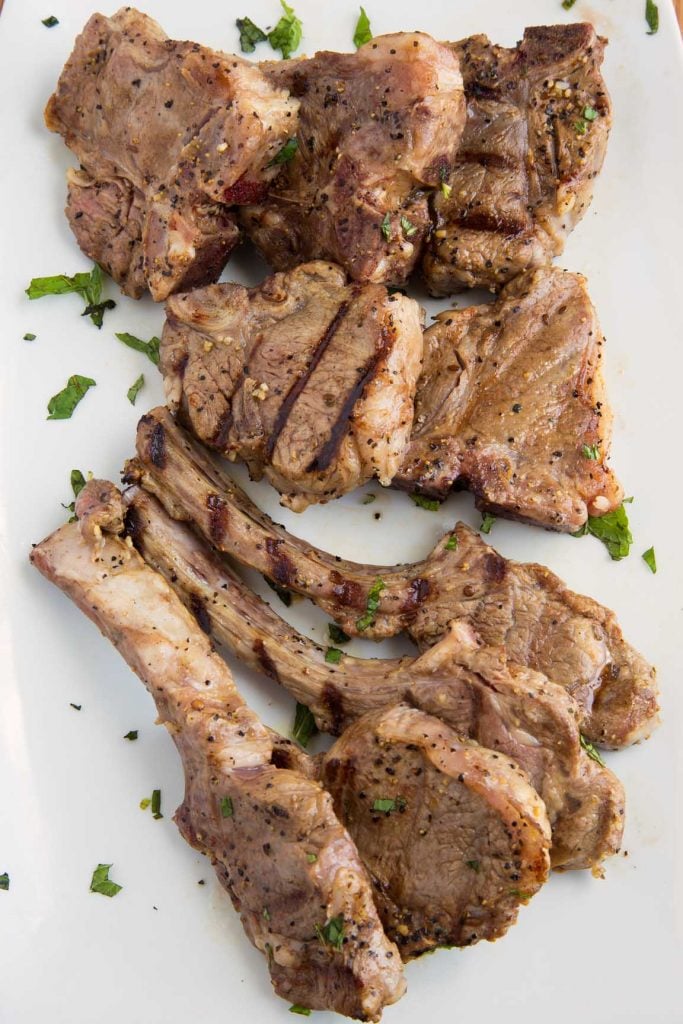 grilled lamb chops on a white platter garnished with chopped parsley