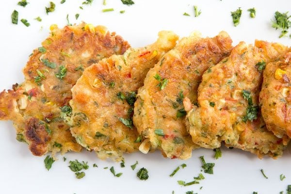  row of homemade corn fritters on a white platter sprinkled with parsley