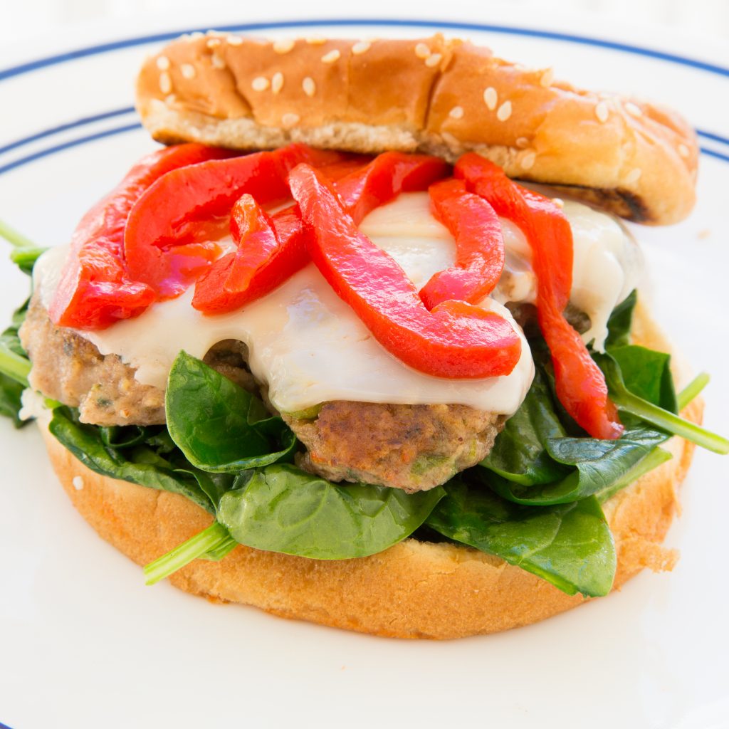 Veggie burger with melted cheese and roasted red peppers with spinach underneath