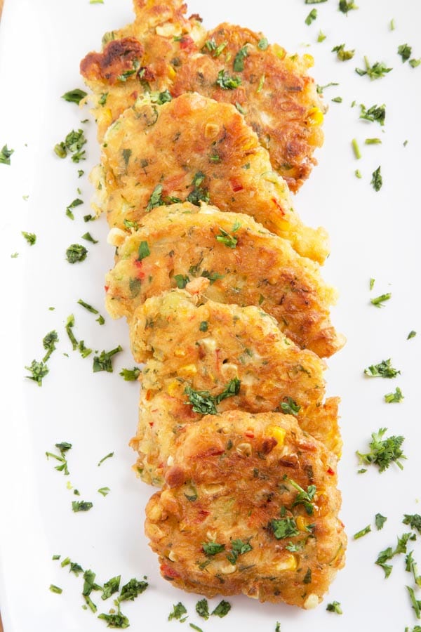 row of homemade corn fritters on a white platter sprinkled with parsley