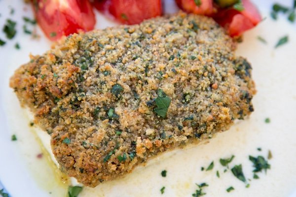 bread crumb crusted halibut and a tomato and olive salad on a white plate