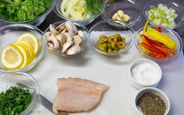 ingredients to make Red Snapper en Papillote in glass bowls and on a white cutting board