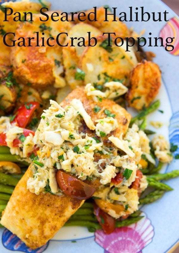pan seared halibut with crab meat and grape tomato halves on a bed of asparagus with roasted potatoes with melted cheddar as the side dish all sitting a blue seashore style plate