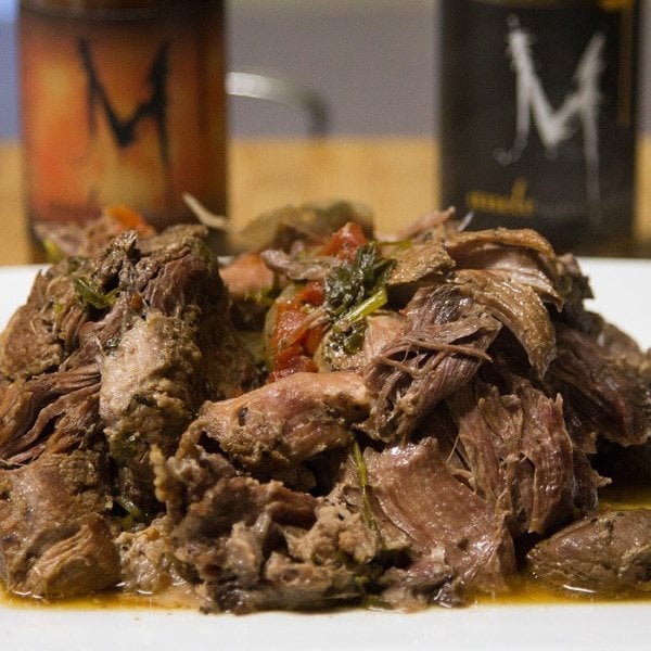 pulled Wild Boar meat on a white cutting board with blurred bottles in the background