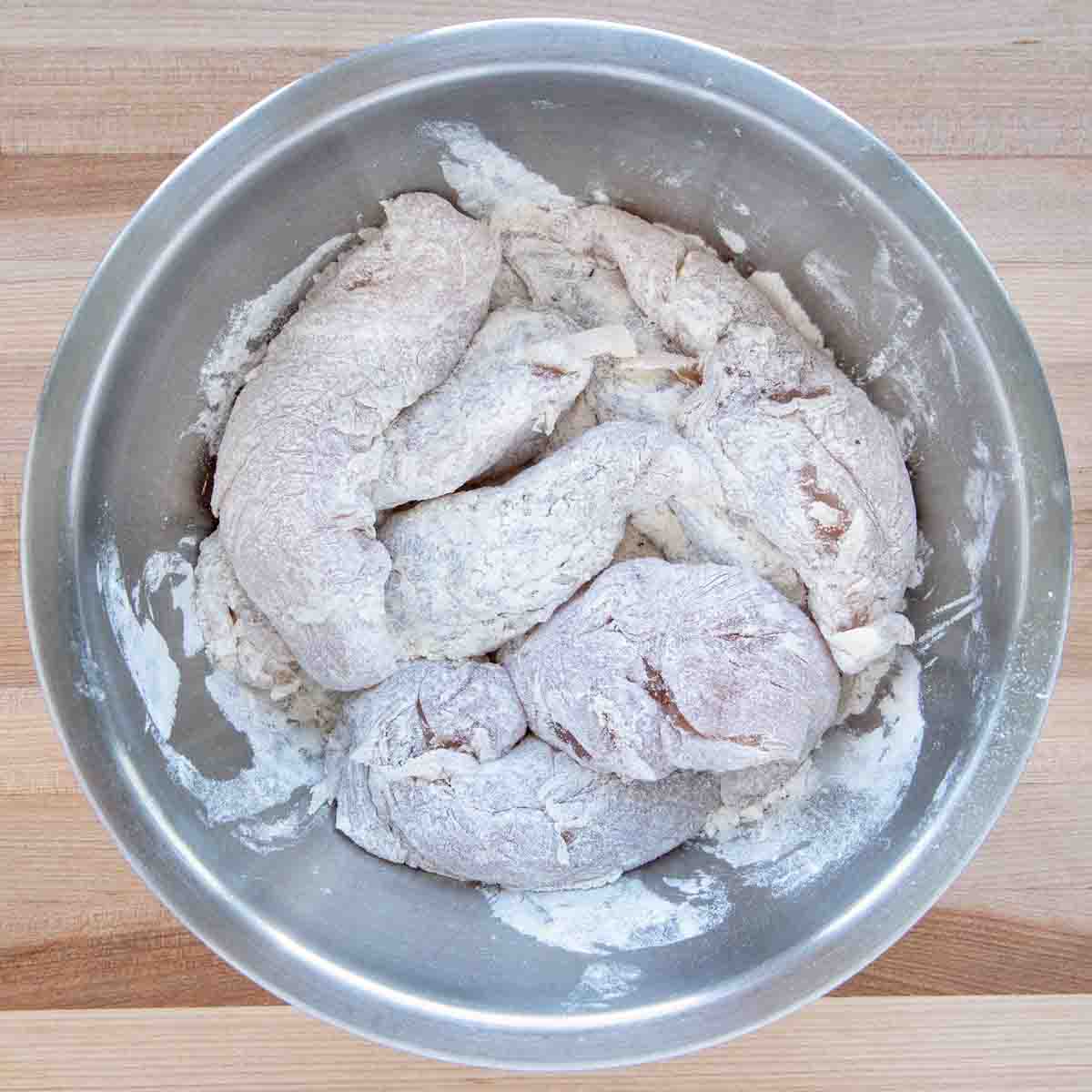 floured chicken tenders in a stainless steel bowl