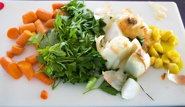 rough cut carrots, parsley and onion (including skin) and oiled garlic cloves on a white cutting board